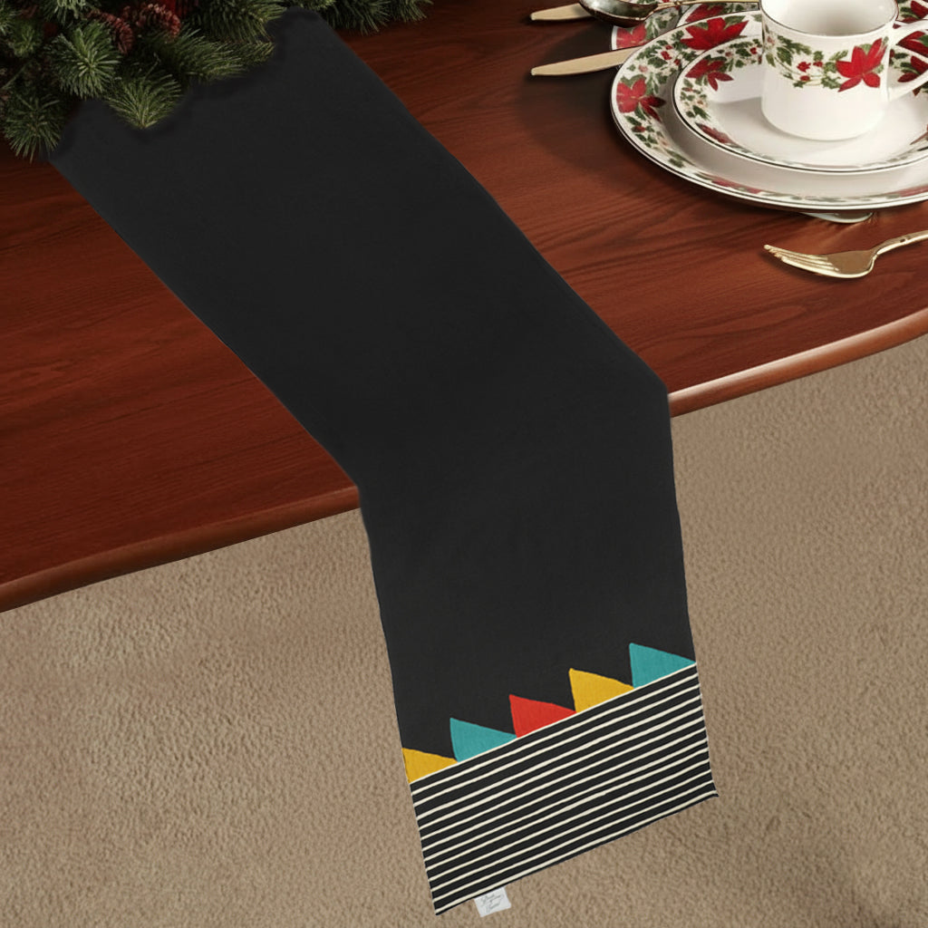 Black cotton table runner with colourful triangles and cream vertical stripes, in Bauhaus-inspired design